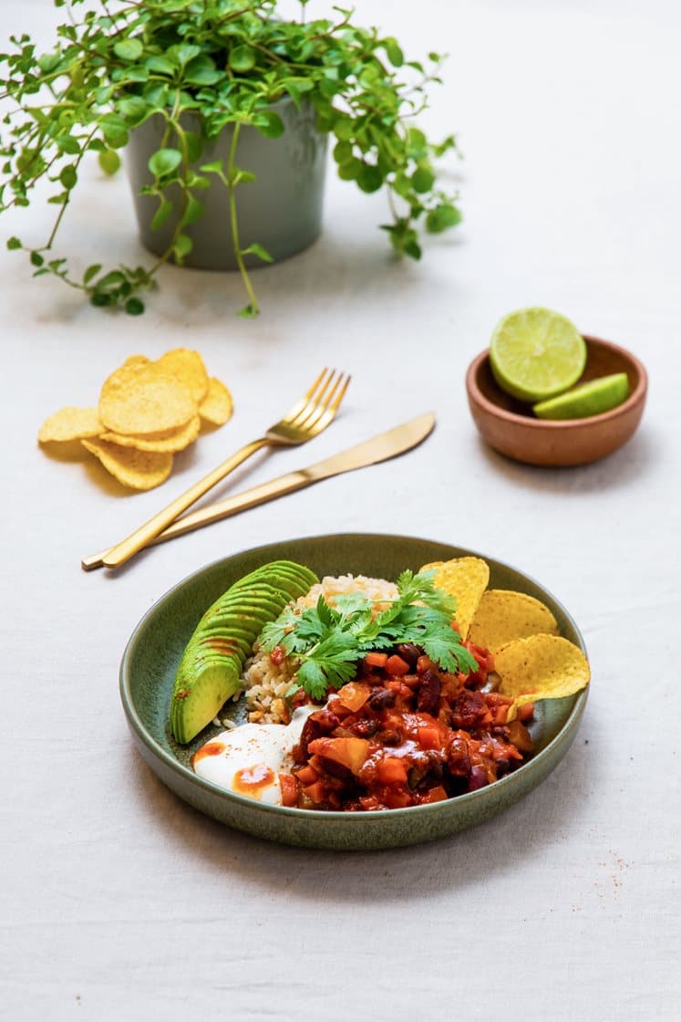 Chili sin carne med sorte bønner og øl, servert med rømme, avokadoskiver og nachochips