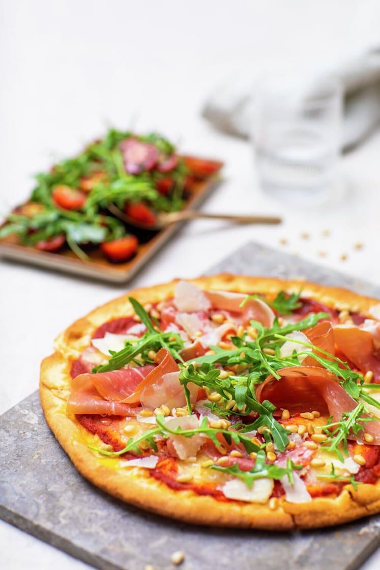 Pizza Parma toppet med ristede pinjekjerner, ruccola og Grana Padano, servert med tomatsalat