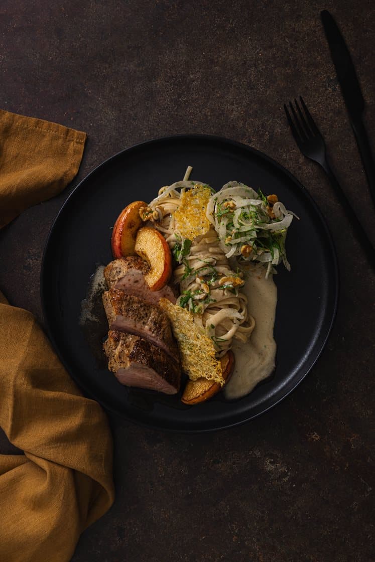 Svinefilet med steinsoppkremet pasta, servert med honningbakt eple, valnøtter og ostechips