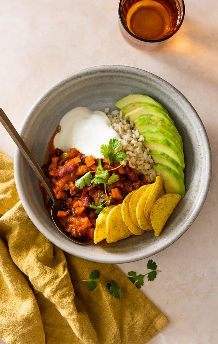 Chili sin carne med sorte bønner og øl, servert med rømme, avokadoskiver og nachochips