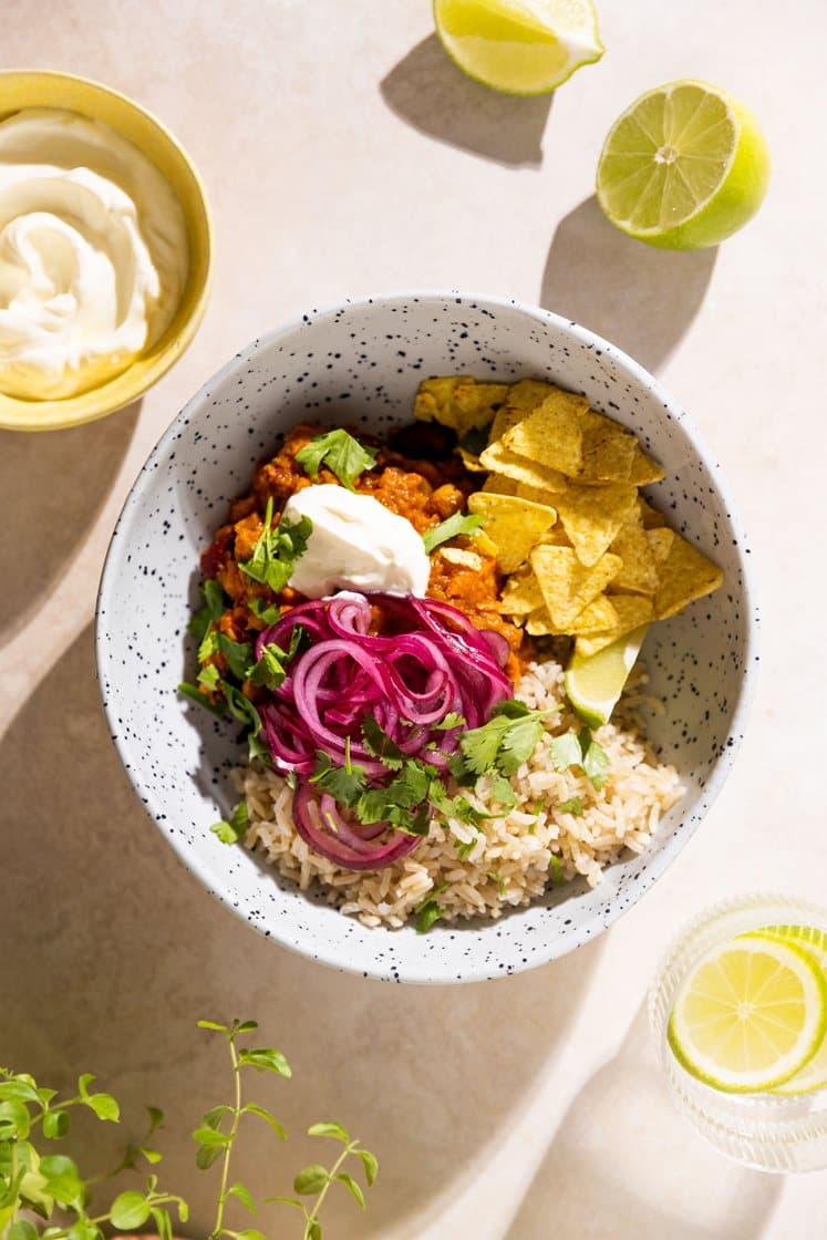 Chili sin carne med fullkornsris, marinert rødløk, tortillachips og lettrømme, servert med lime