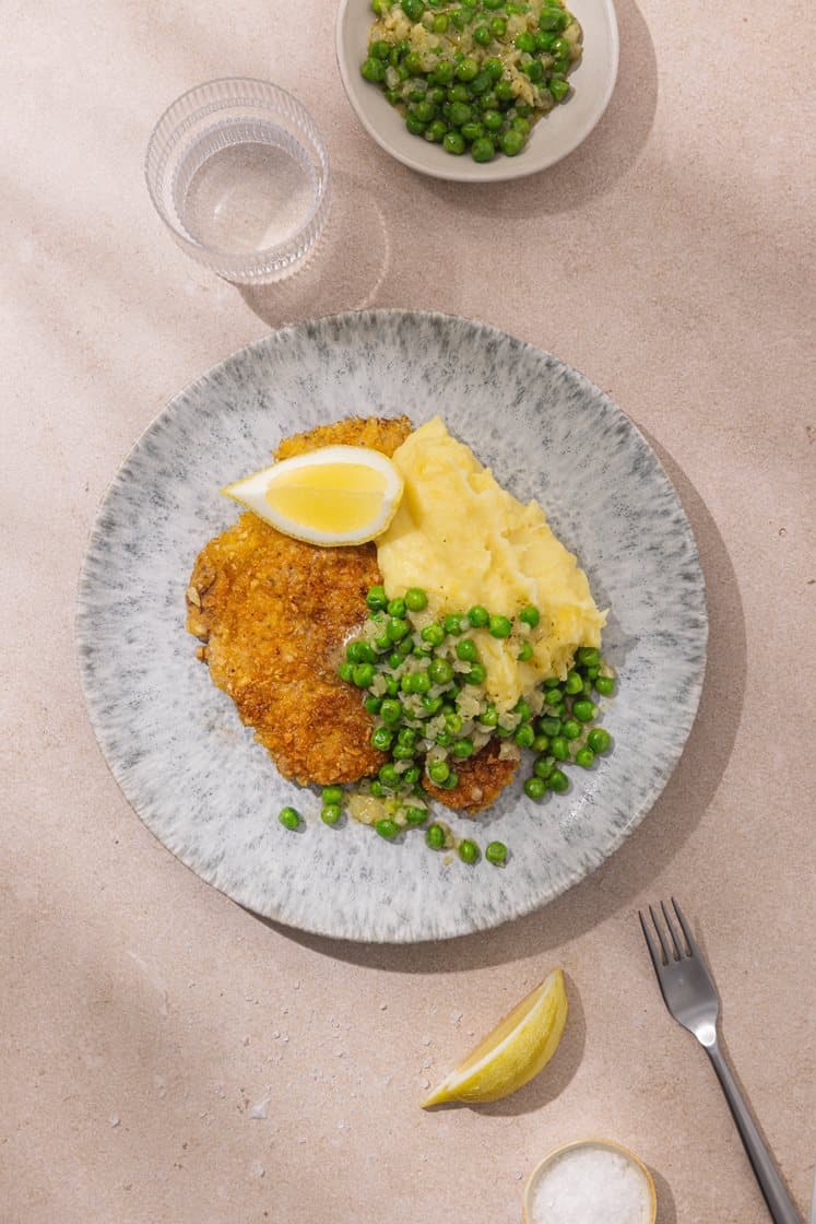Sitronpanerte svineschnitzler og potetpuré, servert med kryddersmør med erter og løk 