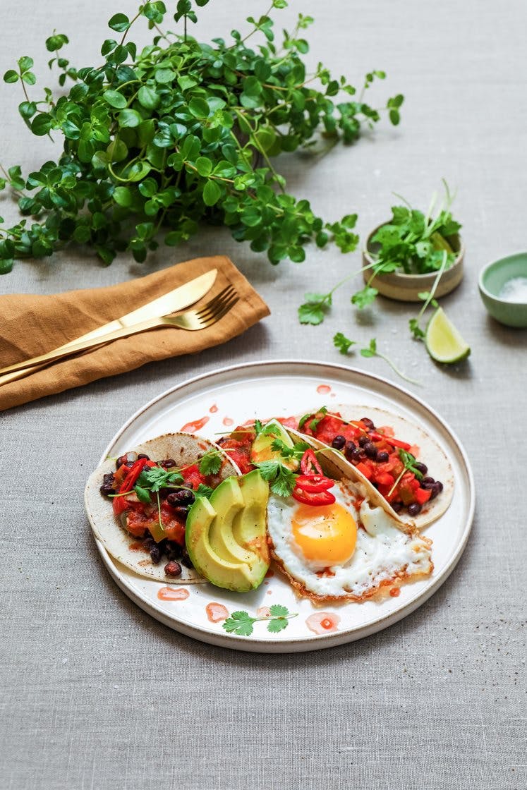Meksikanske huevos rancheros – stekte egg, bønner og tomatsaus, servert med avokado, lime og sprø maistortillaer