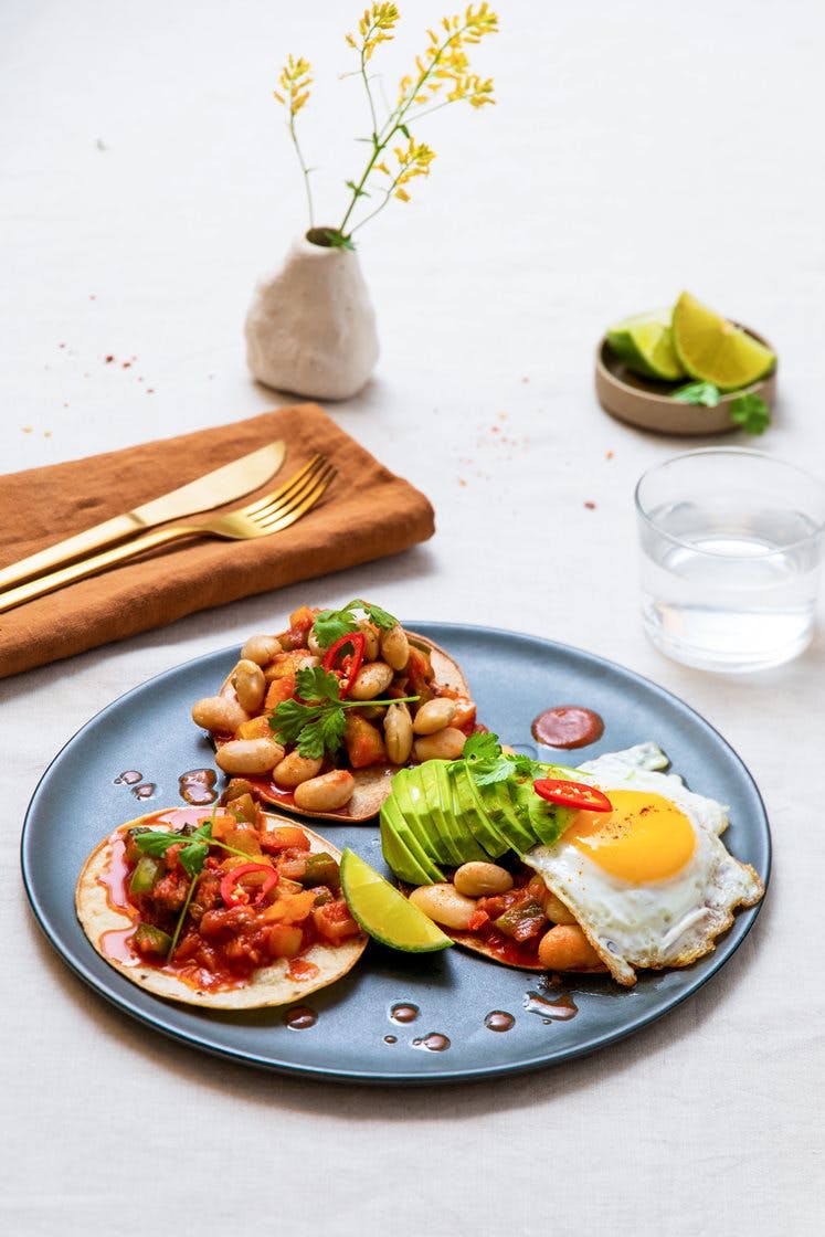 Meksikansk huevos rancheros - Stekte egg, bønner og tomatsaus, servert med avokado, lime og sprø maistortillaer